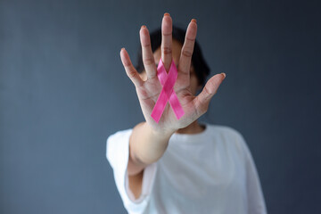 Woman showing pink satin ribbon on her palm covering face. Cancer awareness symbol, women's health, breast cancer day