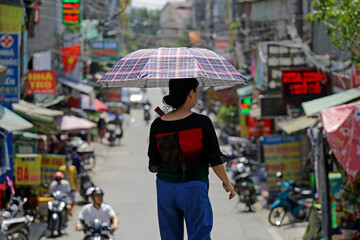 Woman use an umbrella to protects from the hot sun while walking through a street during a severe heat wave in Hanoi, Vietnam.