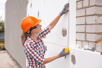 Insulation of the house with polyfoam. The worker is checking with the construction level the...