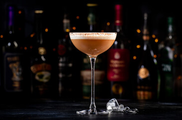 Rattlesnake alcoholic cocktail drink with coffee and cocoa liquor, irish cream, ground coffee and ice in glass, dark bar counter background, bar tools and bottles