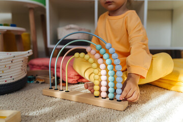 Child sitting on floor playing with wooden Montessori Abacus toy in childrens room.  Early math...