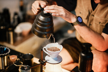 Barista making drip coffee with hot water being poured from a kettle, Ground coffee beans contained in a filter, Make drip coffee, Slow bar coffee.