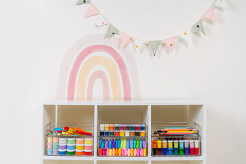 Transparent plastic containers with stationery and supplies for drawing and craft on shelves. White...