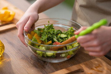 Woman dressing fresh vegetable salad with olive oil in kitchen