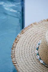 Straw hat with white and blue shells in the pool with blue water. Summer holiday background.
