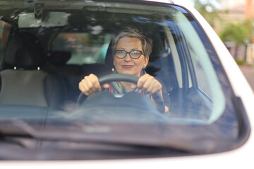 Portrait of a mature woman driving a car through the windshield.