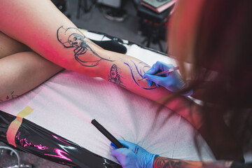 a tattoo master drawing on a client's leg with a blue marker, Freehand technique. High quality photo