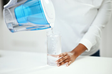 Hands, person and pitcher of filter water, glass and liquid hydration for purification at home. Closeup, thirsty woman and pouring healthy aqua beverage for nutrition, drinking and clean filtration