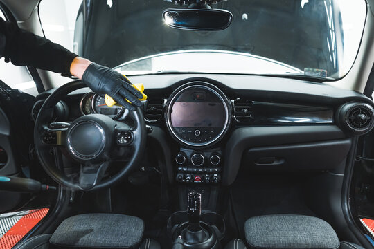Cleaning black interior of a car in a car detailing studio. Man in protective glove wiping the steering wheel. High quality photo
