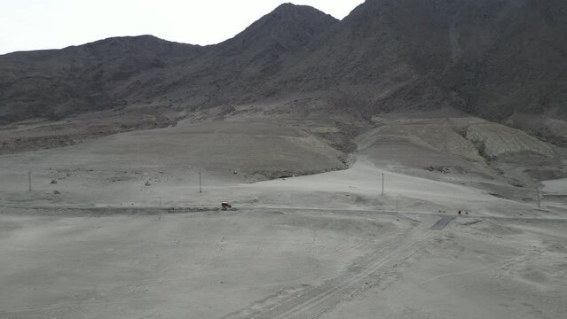 Aerial long shot of a jeep running on Karakoram Highway near Chilas on road to Hunza Valley. This part of highway is surrounded by sand dunes and Rocky Mountains