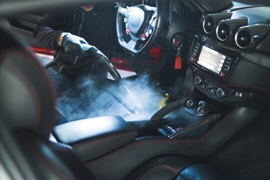 Car service worker cleans interiror with steam cleaner. Steam cleaning of car seats and cockpit. Indoor shot. Professionals at work. High quality photo