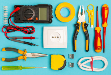 Electrician equipment on blue background with copy space.Top view.Electrician tool set.Multimeter, tester,screwdrivers,cutters,duct tape,lamps,tape measure and wires.Flet lay. © Avocado_studio