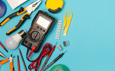 Electrician equipment on blue background with copy space.Top view.Electrician tool set.Multimeter, tester,screwdrivers,cutters,duct tape,lamps,tape measure and wires.Flet lay. © Avocado_studio
