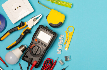Electrician equipment on blue background with copy space.Top view.Electrician tool set.Multimeter, tester,screwdrivers,cutters,duct tape,lamps,tape measure and wires.Flet lay. © Avocado_studio