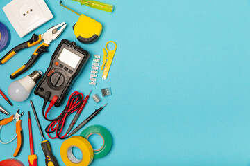 Electrician equipment on blue background with copy space.Top view.Electrician tool set.Multimeter, tester,screwdrivers,cutters,duct tape,lamps,tape measure and wires.Flet lay. © Avocado_studio