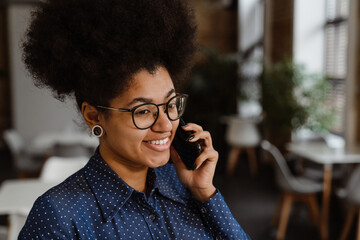 Cheerful african business woman talking on mobile phone while standing in office