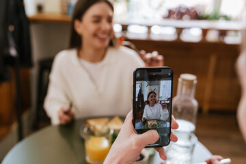 Man taking pictures of his girlfriend with mobile phone while having lunch together in cafe