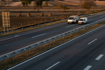 Two minivans are moving on the highway. White delivery van on the highway. White modern delivery small shipment cargo courier van moving fast on motorway road to city urban suburb. 
