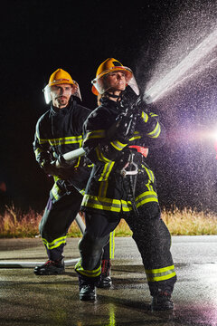 Firefighters using a water hose to eliminate a fire hazard. Team of female and male firemen in dangerous rescue mission. 