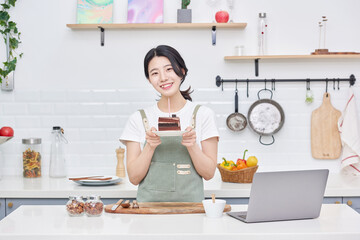 young Asian female model who makes a piece of cake in the kitchen and eats it deliciously