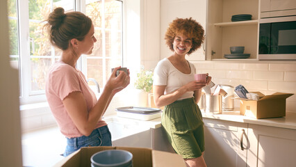 Two Female Friends Or Same Sex Couple Taking A Coffee Break From Unpacking On Moving Day In New Home