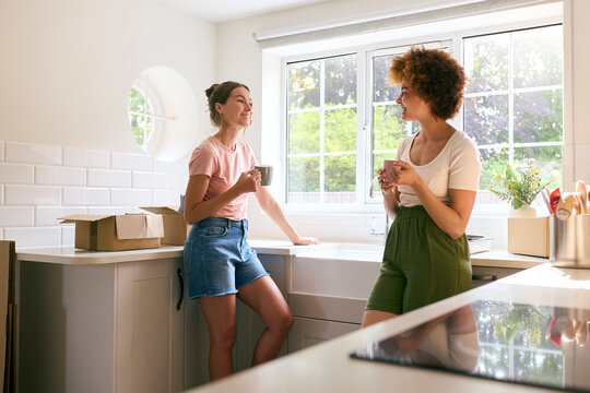 Two Female Friends Or Same Sex Couple Taking A Coffee Break From Unpacking On Moving Day In New Home