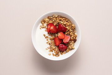 Granola with yogurt and strawberries in white bowl on light beige background with copy space. Top view quick healthy breakfast