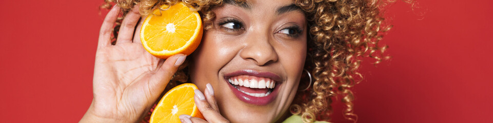 Young black woman with afro curls having fun holding orange