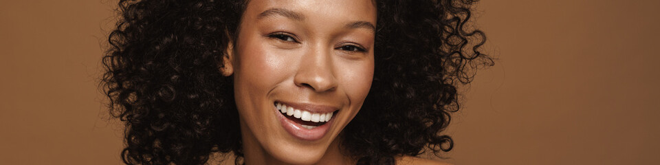 Black shirtless woman with curly hair smiling and using mascara