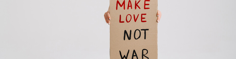 Young woman posing at camera and holding placard with peace message