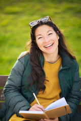 Smiling young woman sitting outside and writing in book
