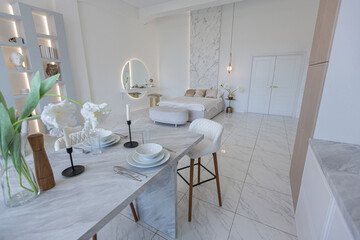 minimalistic light elegant luxury design of a modern spacious studio apartment with kitchen area, bedroom and huge mirror behind the couch. tiles on the floor and high ceiling.