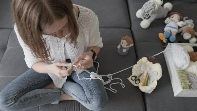 A talented craftswoman with a creative idea intertwines yarn, creating amigurumi that approaches perfection in its appearance and elegance. Sitting and working on the couch at home