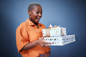 Black woman, gift package and surprise in studio with excited smile, giveaway and blue background....