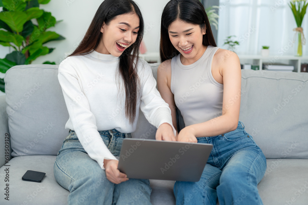 Wall mural two young asian women having fun while shopping online on their laptops on the sofa together in the 