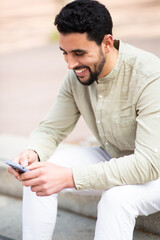 Happy arab guy sitting outside using his mobile phone