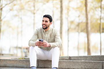 Fototapeta premium Young middle eastern guy sitting outside with mobile phone