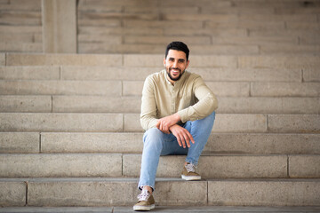 Handsome young arab man sitting on steps and smiling