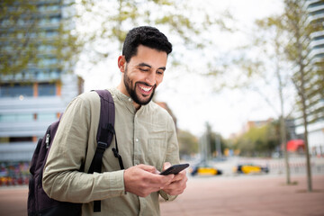 Handsome middle eastern man walking outside with bag using cell phone
