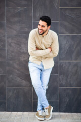 Cheerful young arabic guy standing against black wall with arms crossed