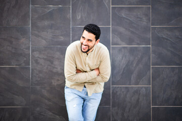 Laughing arabic man leaning against black wall with arms crossed