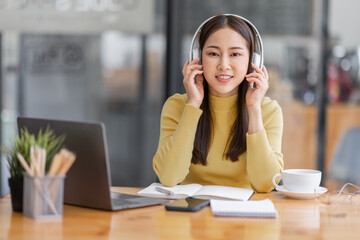 Young adult happy smiling Asian student or business woman wearing headphones talking on online chat meeting using laptop in office or campus, asian female student wear glasses learning remotely.