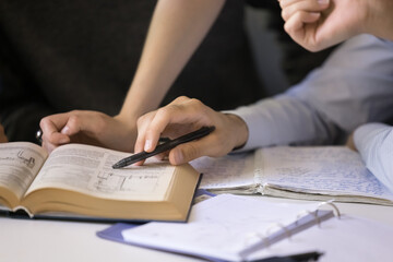Close up of open scientific textbook and hands of students pointing at page. Group of classmates reading, discussing book together, meeting at table for studying in team, getting knowledges