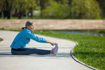 Woman sittingon the yoga mat in the park and doing stretching