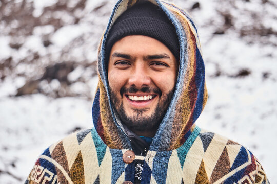 Smiling young man in cap and hood standing on snowy terrain