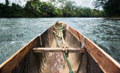Wooden travel boat with rope on flowing water near green trees