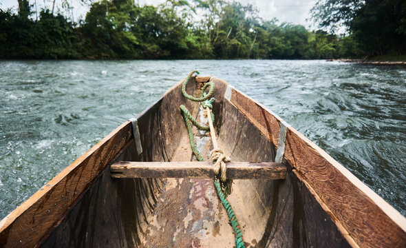 Wooden travel boat with rope on flowing water near green trees - Powered by Adobe