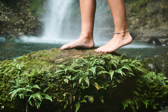 Unrecognizable woman standing on rock with grass plants near waterfall