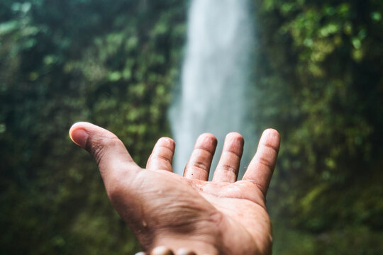 Hand of person open towards forest waterfall