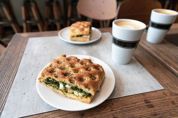  Sandwiches on a white plate and a cup of caffe latte or cappuccino on a table in a cafe.